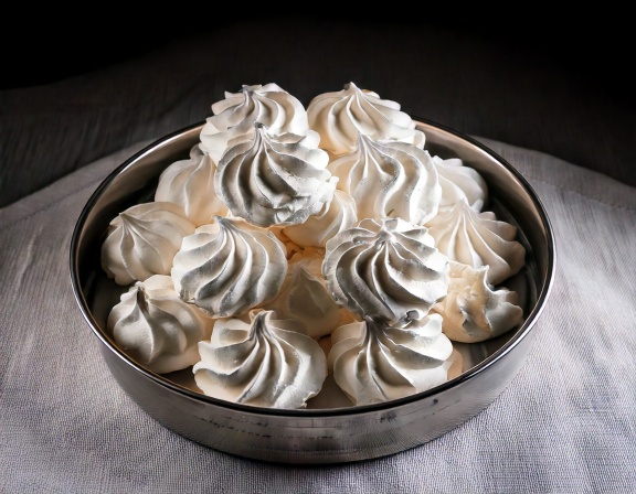 Suspiros brancos modelados em formato de gota, assados e dispostos sobre papel manteiga.