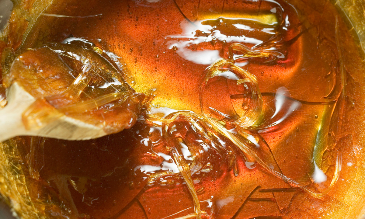 Calda de caramelo lisa e brilhante em tom âmbar, sendo derramada de uma colher em uma tigela.