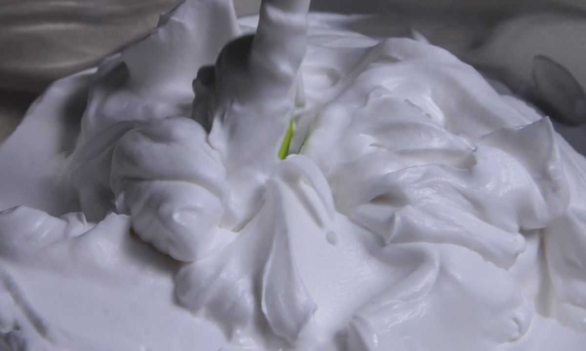 Bolo decorado com creme branco usando bico de confeitar, mostrando detalhes nítidos e textura firme.